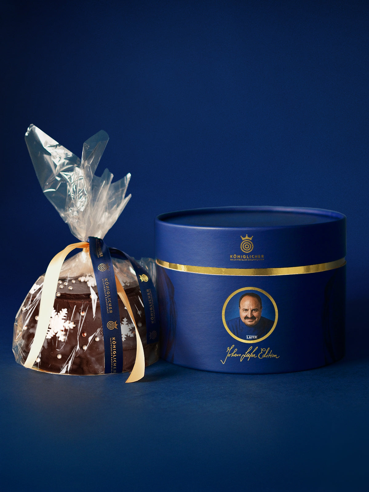 Baumkuchen der Johann Lafer Edition in Klarsichtfolie neben der blauen Geschenkdose