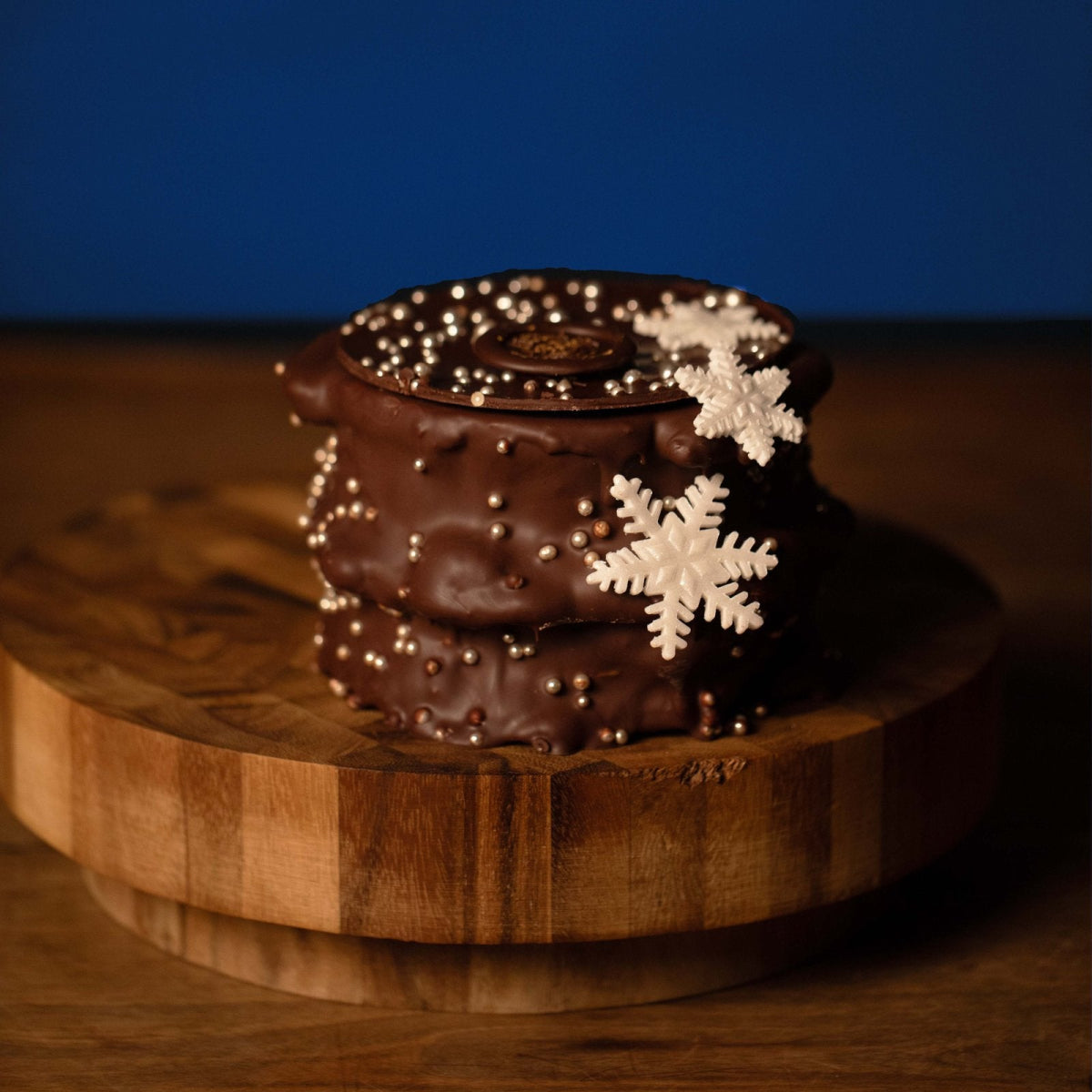Lafers Winteredition – Baumkuchen mit Zartbitterschokolade, Schneeflocken und Perlendekor auf einem Holzbrett